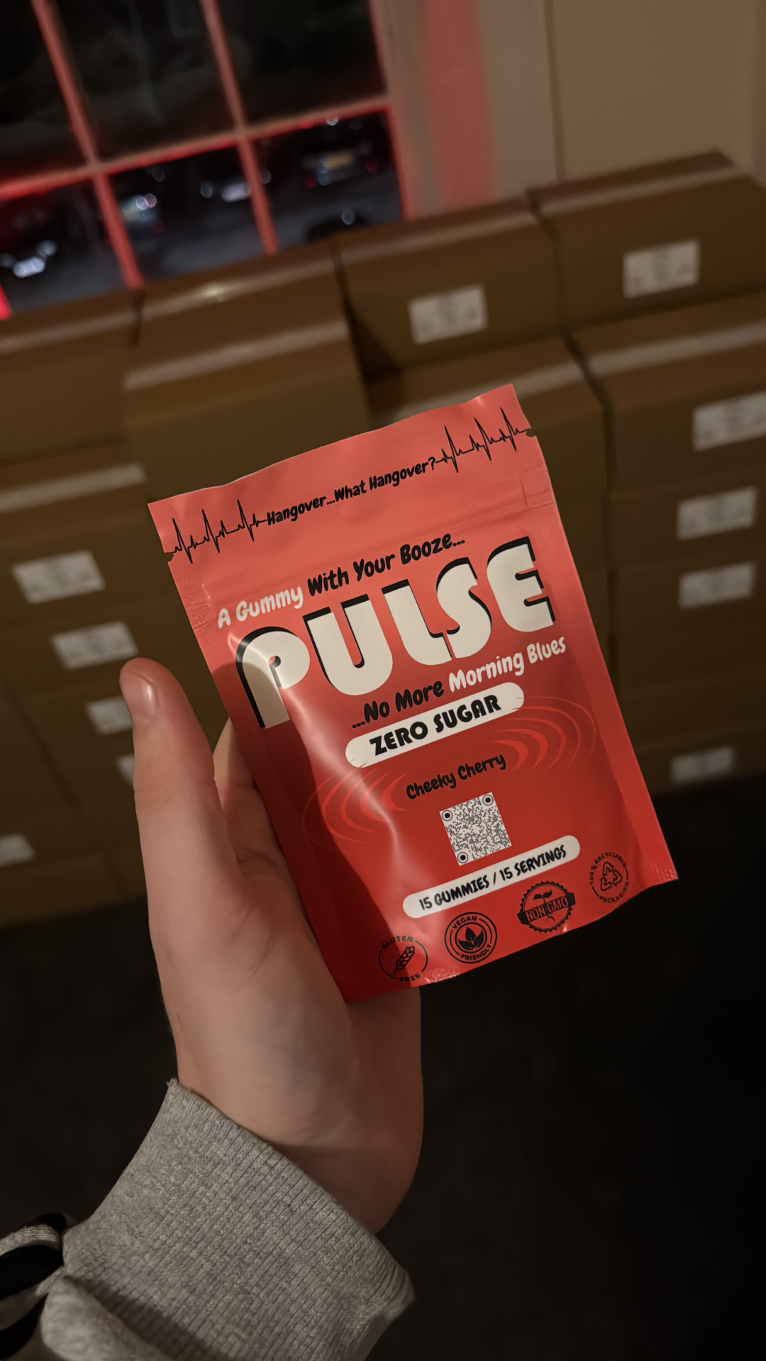 Hand holding a PULSE pouch in front of stacked shipping boxes