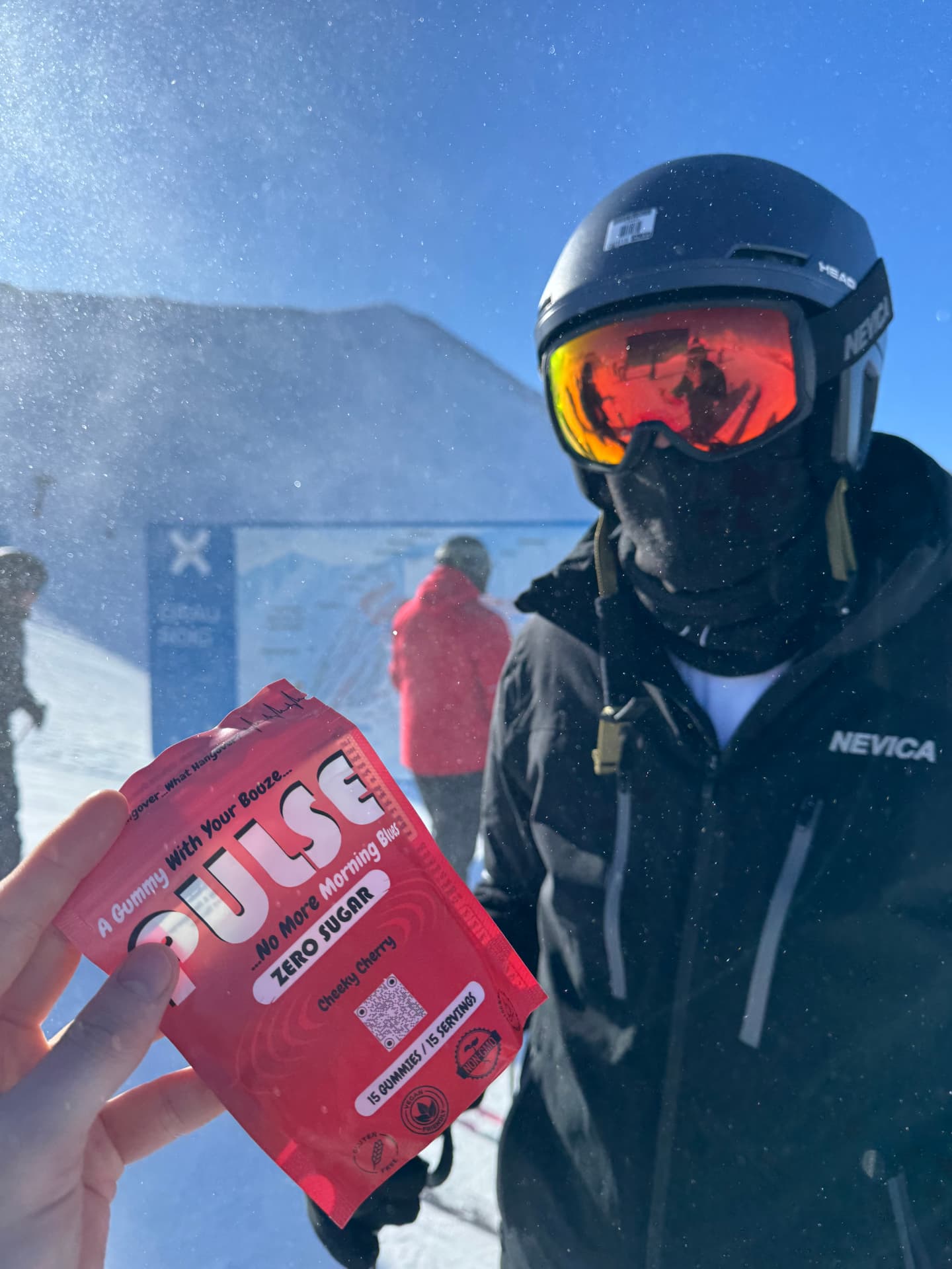 Skier in goggles holding a Cheeky Cherry PULSE pouch in the snow